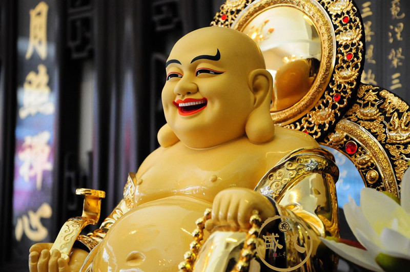 Phật Di Lặc: mập mạp, bụng to, mặt tươi cười hoan hỷ, tay trái cầm xâu chuỗi, tay phải cầm gậy ngọc Như Ý-biểu tượng của cát tường, thịnh vượng